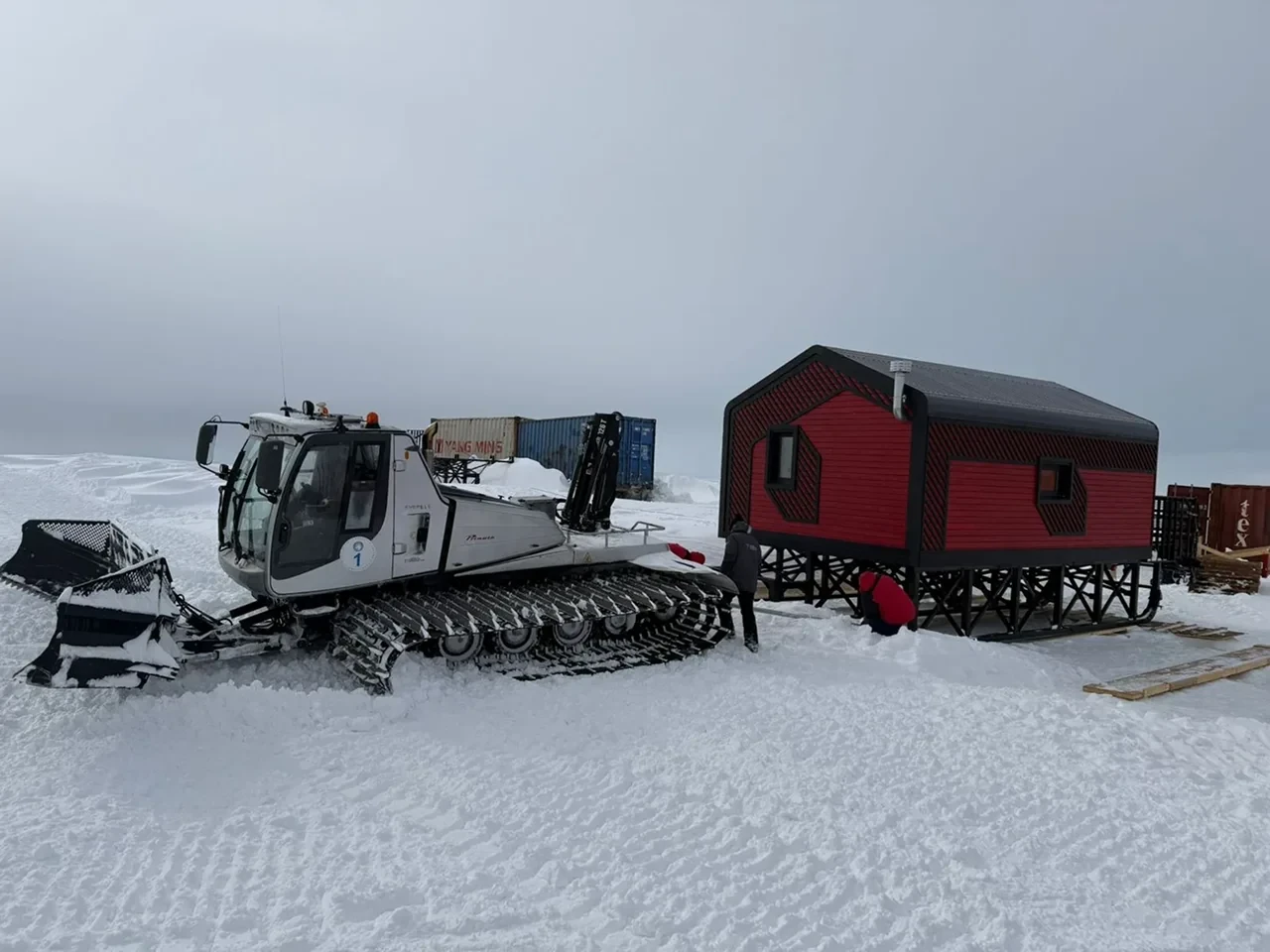 Красный дом Sorena House на снегу рядом с гусеничной техникой